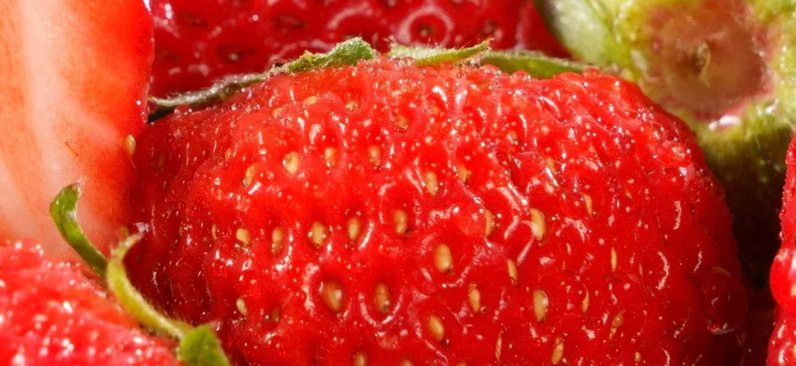HiRezGo: Fotoğrafları Sıkıştırmadan Paylaşmanın Yeni Yolu 7 Close-up of a ripe, red strawberry showing its textured surface, small yellow seeds, and green leafy top, with sections of other strawberries visible around the edges.
