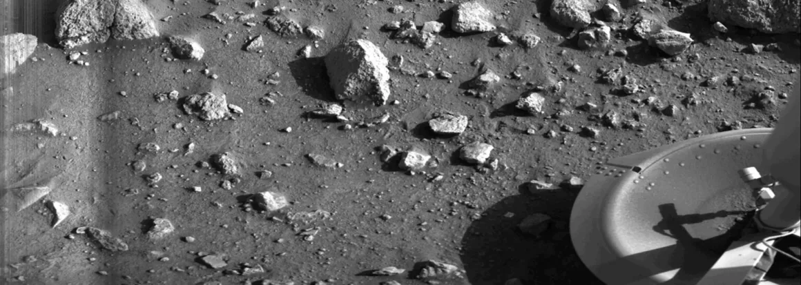 Mars'ta Çekilen İlk Fotoğrafın Üzerinden 50 Yıl Geçti 1 Viking 1 tarafından 20 Temmuz 1976'da Mars yüzeyinden çekilen tarihteki ilk fotoğraf.
Mars'ın taşlarla kaplı, tozlu ve kayalık yüzeyini gösteren siyah-beyaz fotoğraf; sağ alt köşede Viking 1'in iniş ayağı görülüyor.