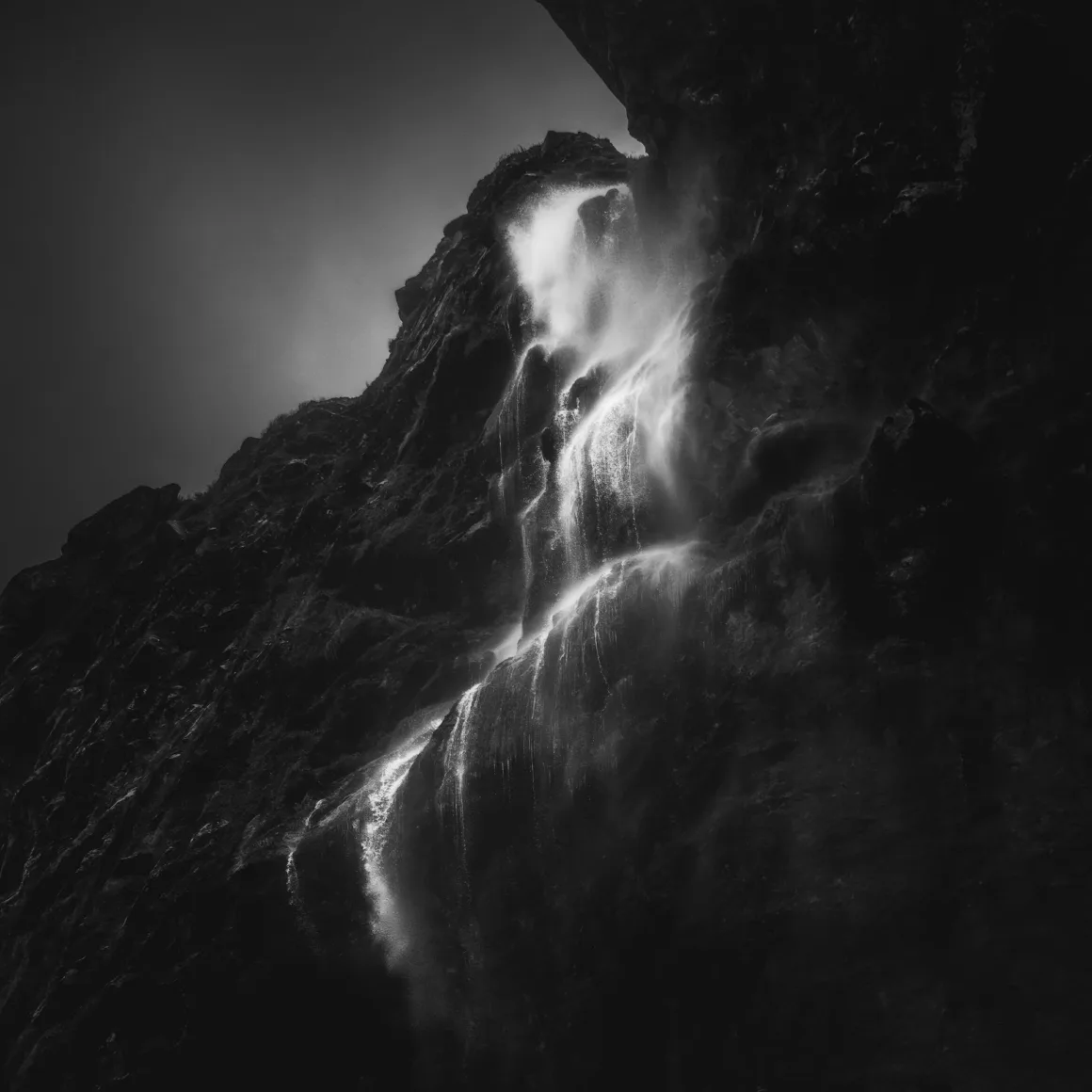 Michael Shainblum, Yeni Zelanda'nın Olağanüstü Güzelliğini Yeniden Yorumluyor 12 Sarp ve koyu renkli kayalık bir yüzeyden dökülen şelalenin dramatik siyah beyaz fotoğrafı. Yükselen su buharı ve güçlü ışık-gölge kontrastı gizemli bir atmosfer oluşturuyor.