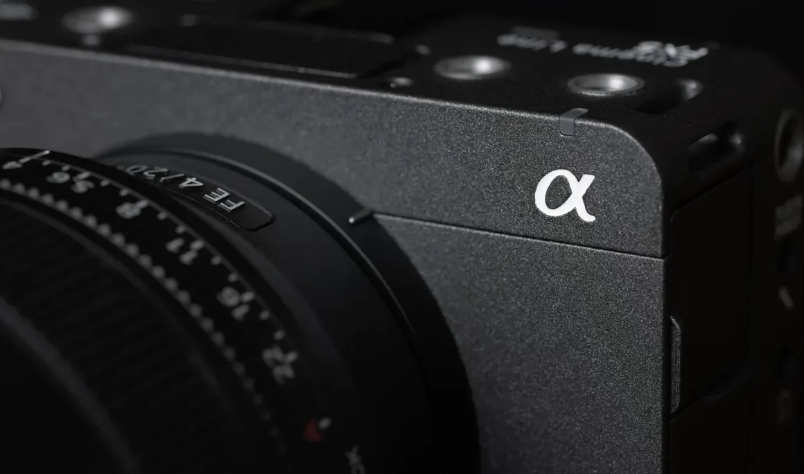 Sony FX5 Neden Sony'nin Bugüne Kadarki En Önemli Sinema Kamerası? 9 Dokulu gövdesi, objektifi ve ön köşesindeki beyaz Alpha (α) logosu görülen siyah Sony Alpha serisi fotoğraf makinesinin yakın plan görüntüsü.