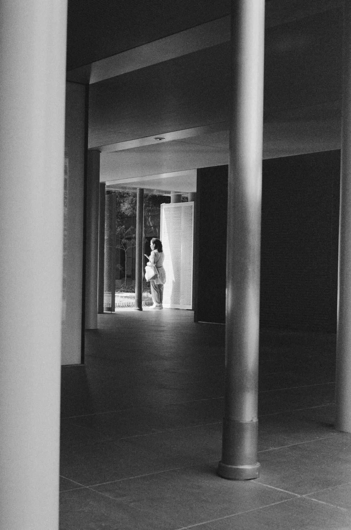 Contax G2 Efsanesi Boşuna Değil: Bu Kamera Harika 26 A person stands in a sunlit corridor framed by large, dark pillars, looking at a mobile device.