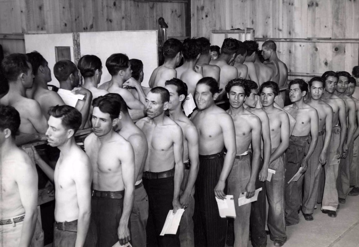 ABD’nin Yüz Yıllık Sınır Dışı Tarihi Fotoğraflarla Ortaya Çıkıyor 22 Ahşap bir binanın içinde, çoğu ellerinde küçük beyaz kâğıtlar tutan üstsüz erkekler tıbbi ya da fiziksel muayene için sırada bekliyor.