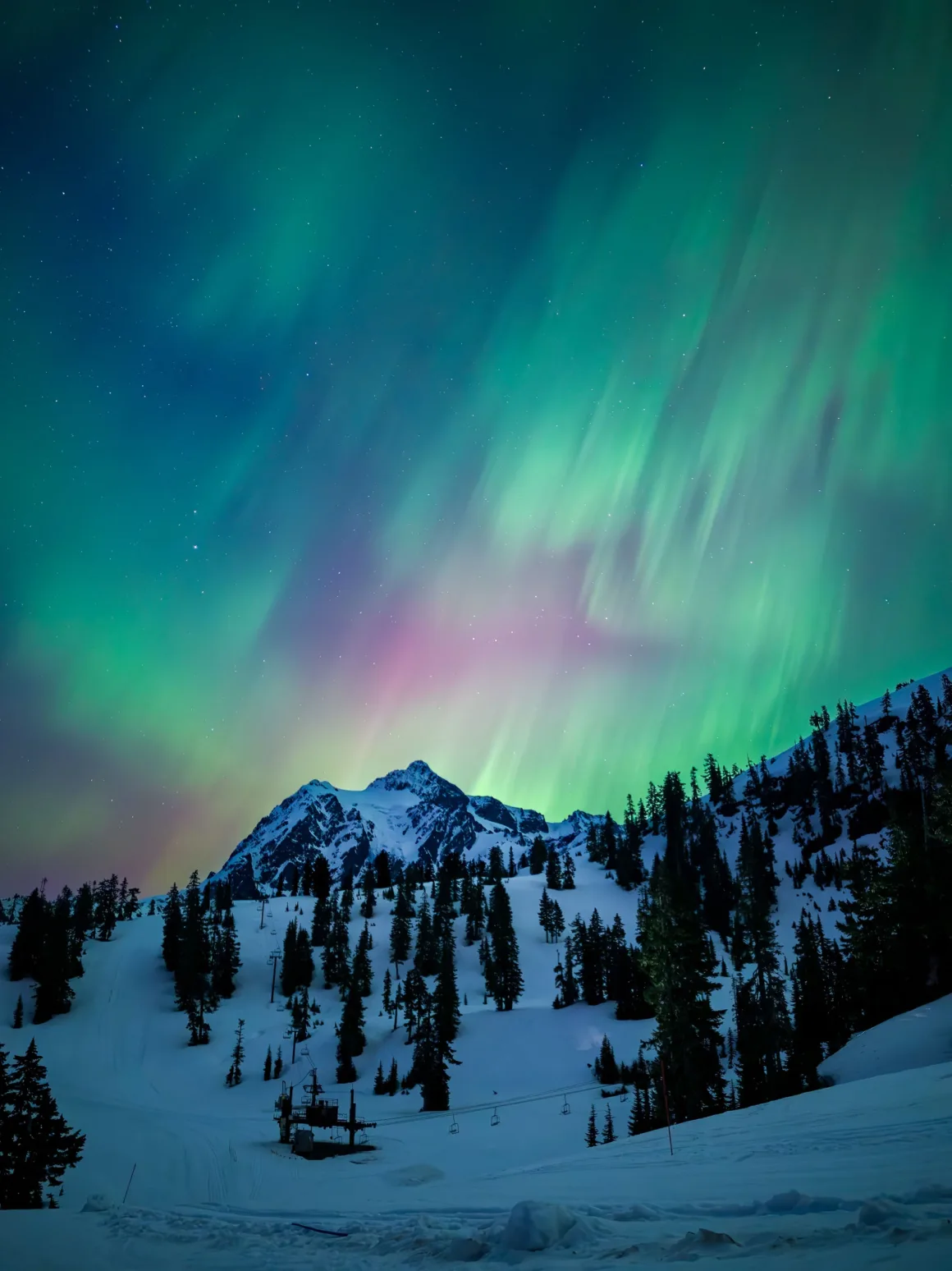 Dünyanın En Karanlık Gökyüzlerinin Güzelliğini Yansıtan 31 Ödüllü Fotoğraf 22 Vibrant green and purple aurora borealis illuminate the night sky above a snow-covered mountain slope with pine trees and a ski lift.