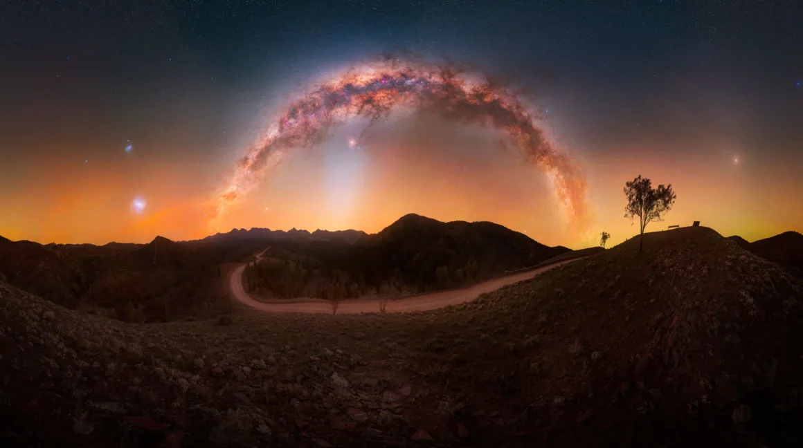 Dünyanın En Karanlık Gökyüzlerinin Güzelliğini Yansıtan 31 Ödüllü Fotoğraf 4 A panoramic view of the Milky Way arching over a dark, hilly landscape with a dirt road and a lone tree on a ridge.
