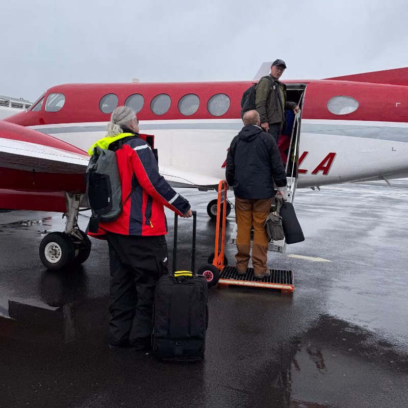Scoresby Sund’da Işıklar Söndüğünde: Arktik’te Tam Güneş Tutulması 17 Three people board a small red and white airplane on a wet tarmac, with one person standing on a portable step ladder.