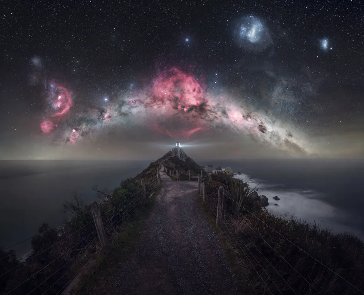 Dünyanın En Karanlık Gökyüzlerinin Güzelliğini Yansıtan 31 Ödüllü Fotoğraf 14 A lighthouse sits at the end of a narrow, fenced path overlooking the ocean beneath a vibrant, star-filled night sky.
