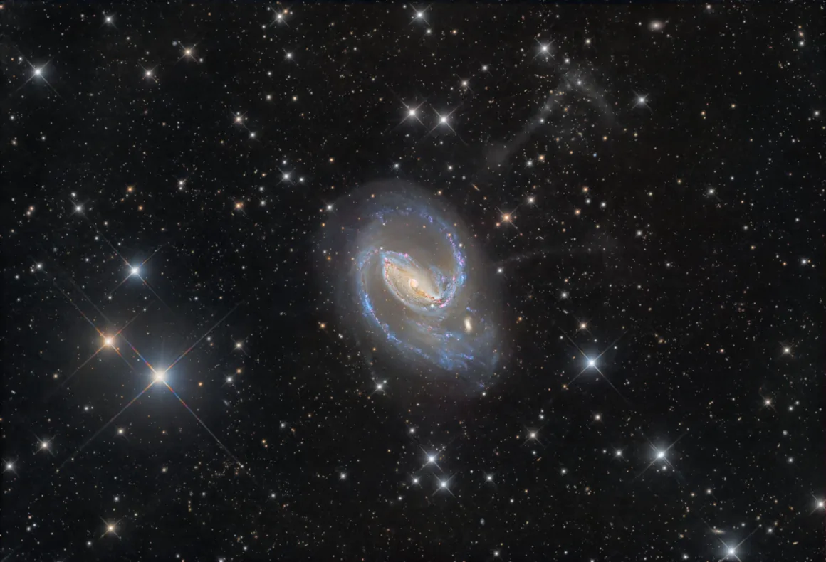 Dünyanın En Karanlık Gökyüzlerinin Güzelliğini Yansıtan 31 Ödüllü Fotoğraf 20 A barred spiral galaxy with bright blue star-forming regions and a glowing central bar sits against a dense field of stars.