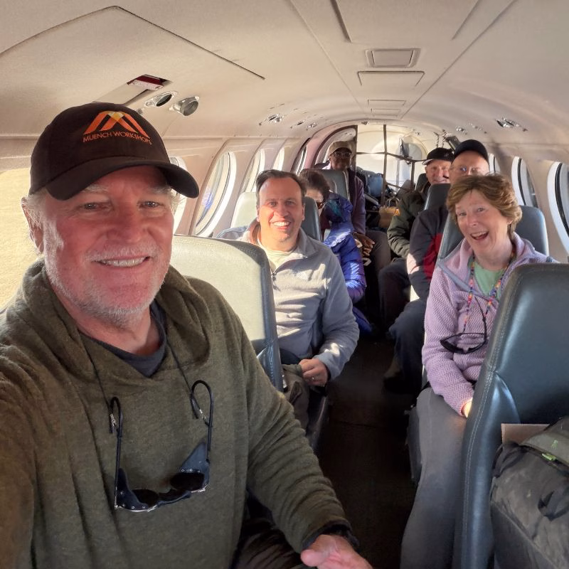 Scoresby Sund’da Işıklar Söndüğünde: Arktik’te Tam Güneş Tutulması 18 A group of people smiling inside the cabin of a small aircraft, with a man in a baseball cap taking a selfie in the foreground.