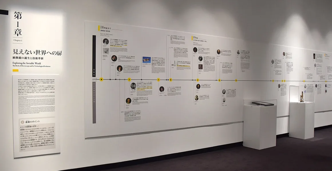 Nikon, 101 Yıllık Mikroskop Mirasını Fotomikrografinin Gizli Dünyasıyla Kutluyor 3 Bir müze sergisi duvarında “Görünmez Dünyayı Keşfetmek” başlıklı uzun bir zaman çizelgesi, tarihsel metinler, portreler ve mikroskopların sergilendiği iki kaide yer alıyor.