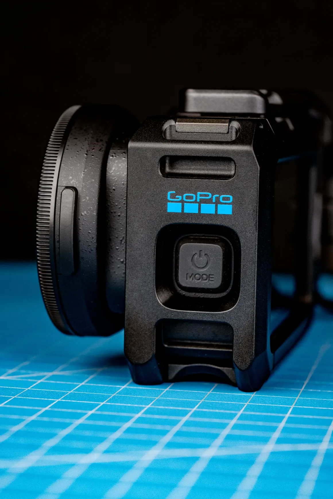 GoPro Mission 1 Pro ILS İncelemesi: Yenilikçi Ama Kime Göre? 34 Güç düğmesi görünen siyah GoPro kamera kafesi, mavi ızgaralı kesim matı üzerinde duruyor.