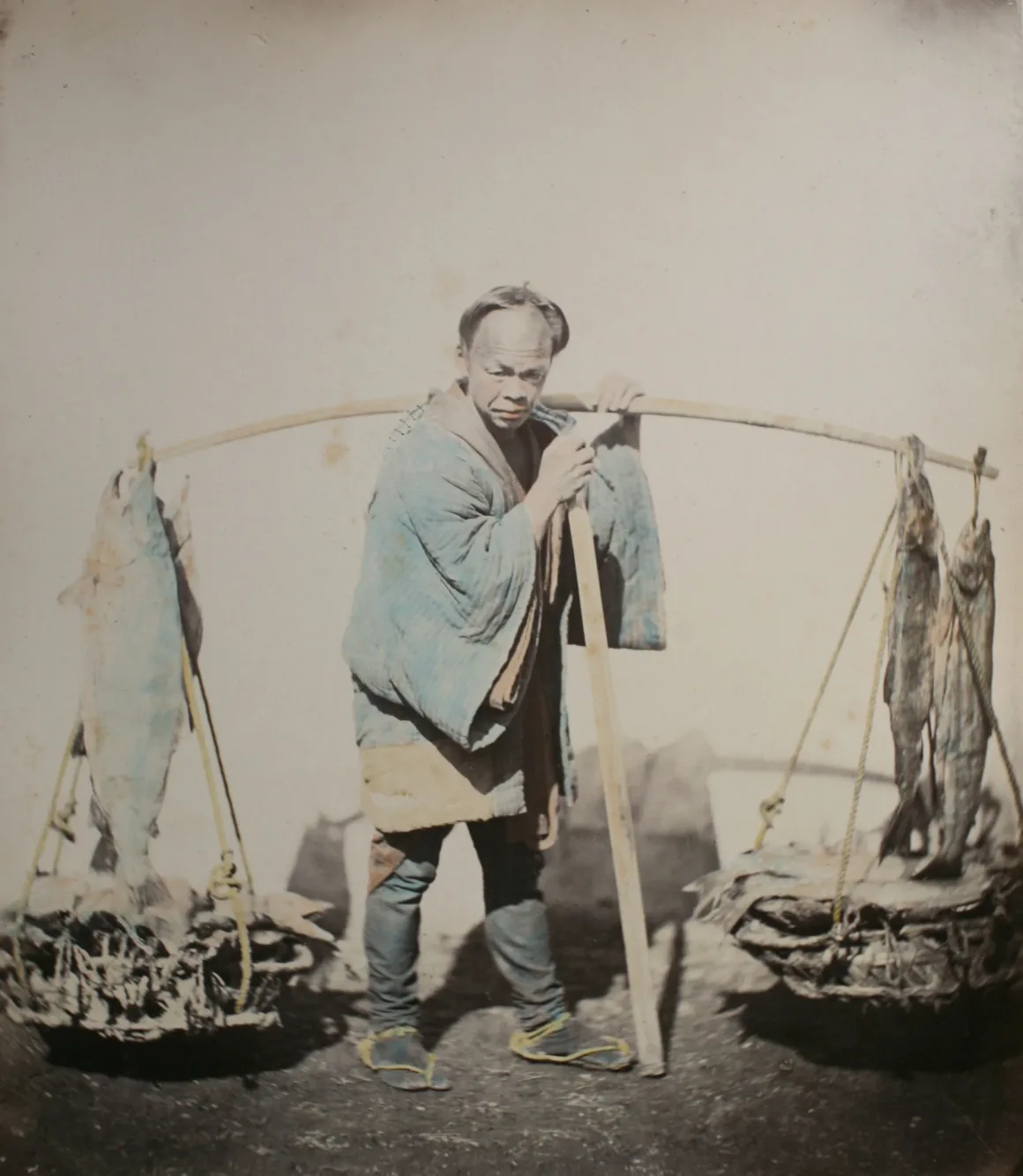 Fotoğrafçı, Japonya’nın Unutulmuş 19. Yüzyıl Fotoğraflarını Buldu ve Bugün Yeniden Yorumladı 18 Mavi kimono giyen balık satıcısı, omzundaki bambu sırığın iki ucuna asılı balık sepetlerini taşıyor.