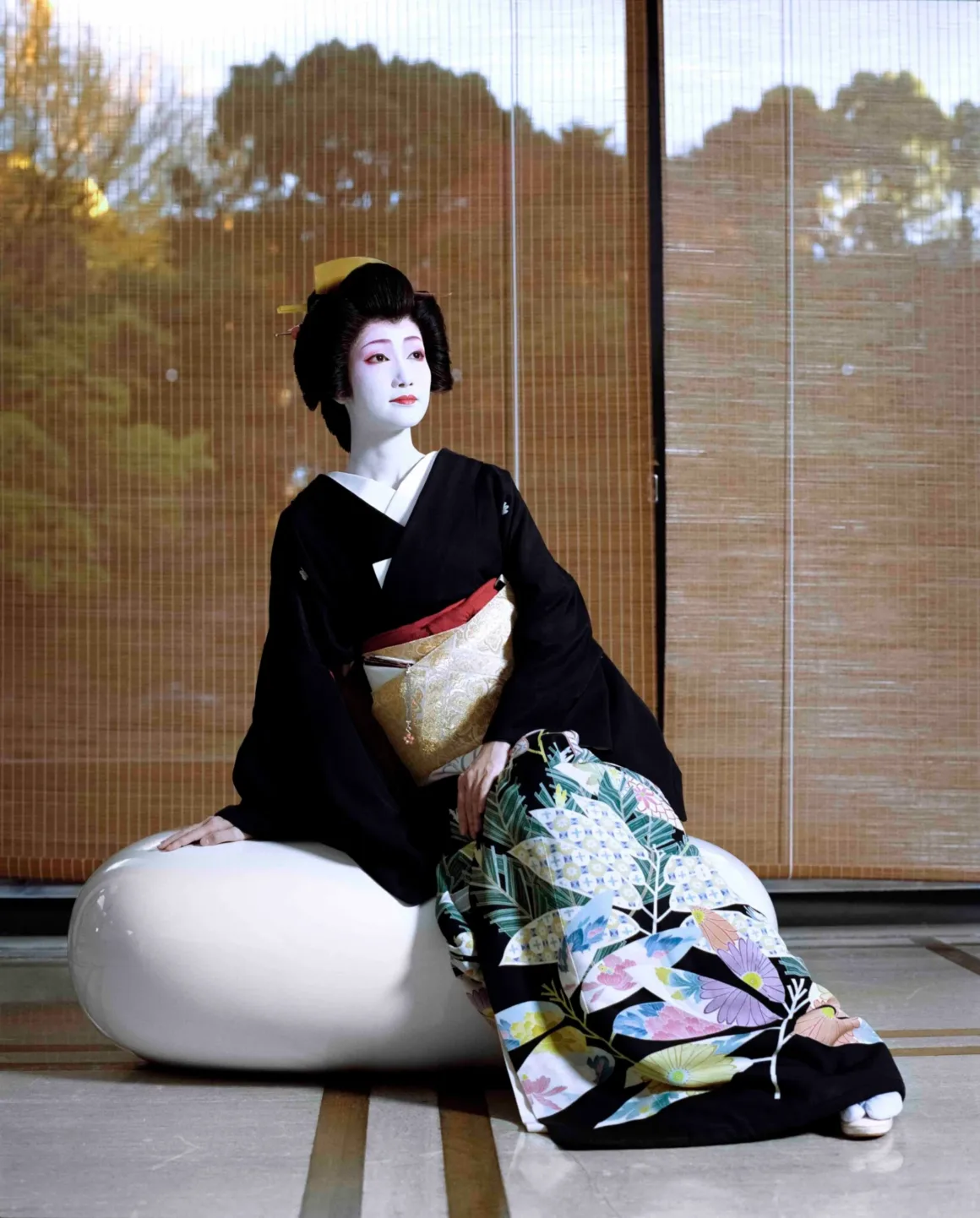 Fotoğrafçı, Japonya’nın Unutulmuş 19. Yüzyıl Fotoğraflarını Buldu ve Bugün Yeniden Yorumladı 29 Geleneksel geyşa makyajı ve çiçek desenli siyah kimonosuyla Suzume, bambu perdelerin önünde oturuyor.