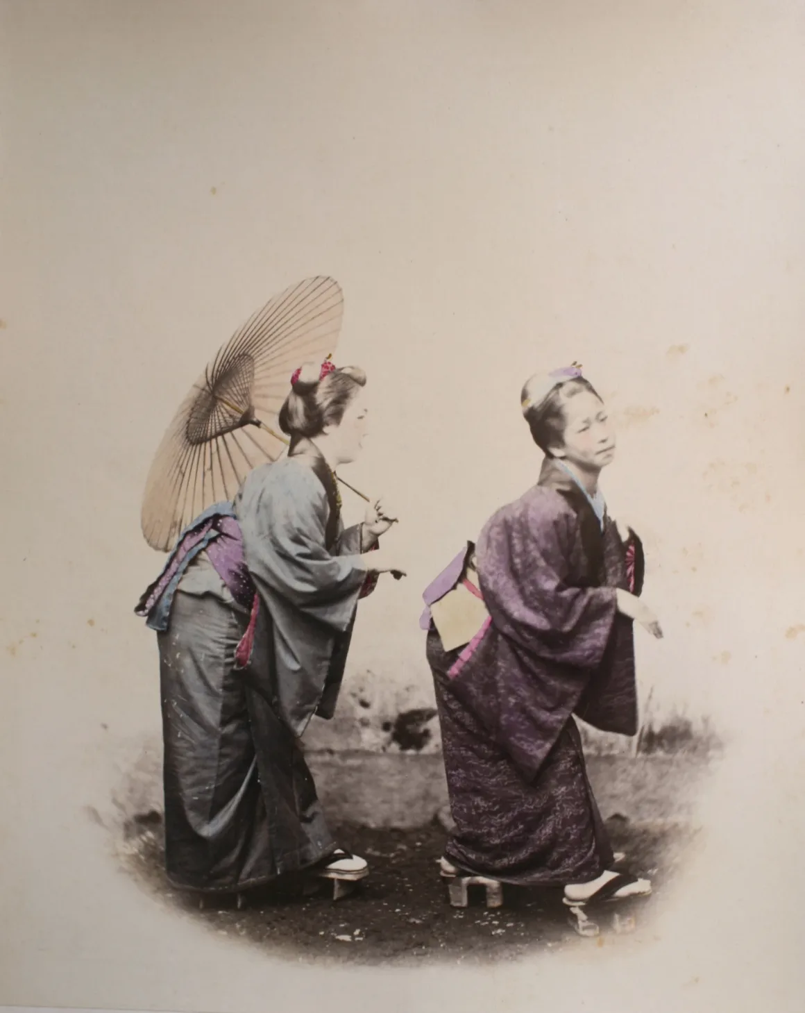 Fotoğrafçı, Japonya’nın Unutulmuş 19. Yüzyıl Fotoğraflarını Buldu ve Bugün Yeniden Yorumladı 16 Geleneksel kimono ve geta sandalet giyen iki Japon kadın, içlerinden biri kâğıt şemsiye tutarken toprak yolda duruyor.