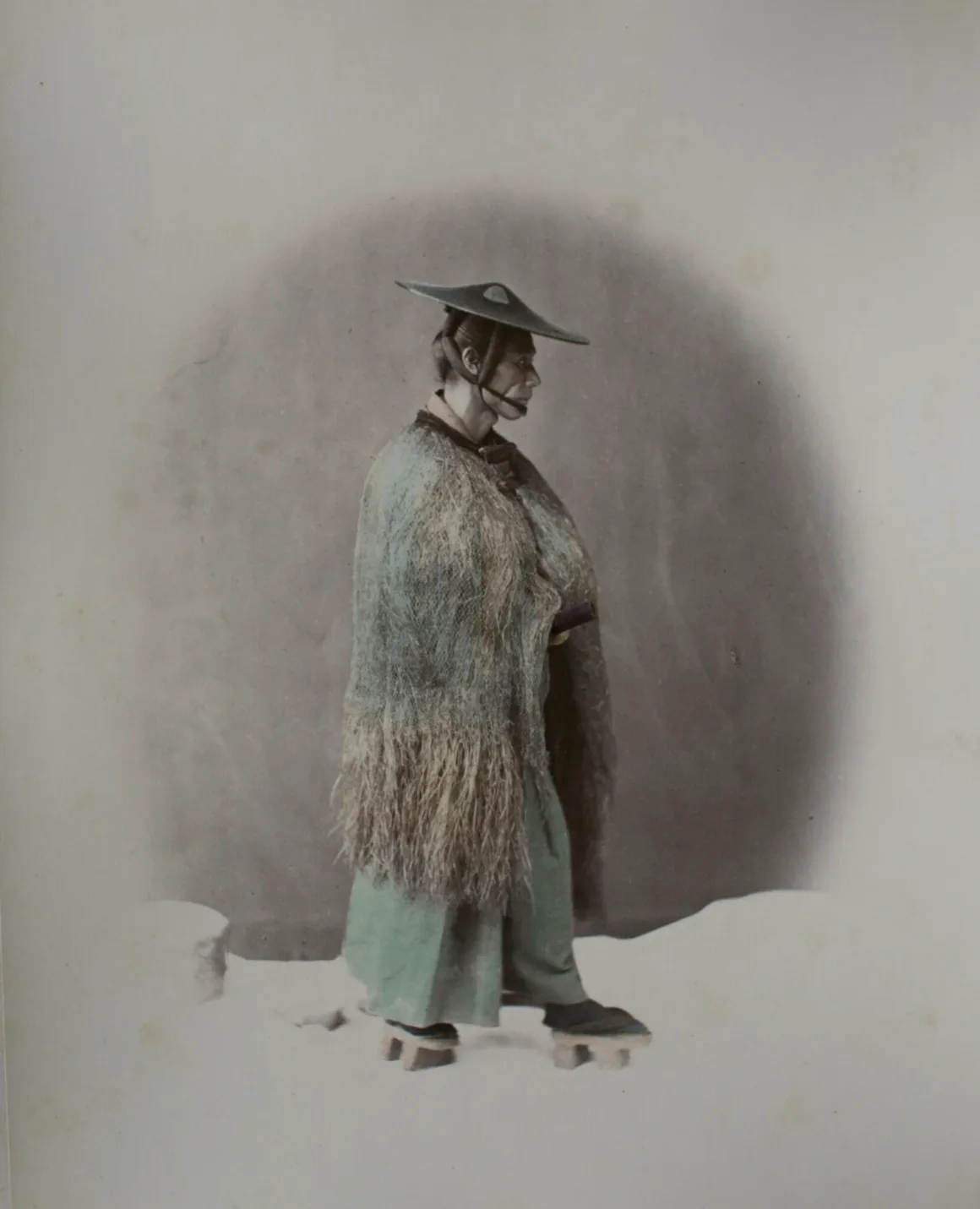 Fotoğrafçı, Japonya’nın Unutulmuş 19. Yüzyıl Fotoğraflarını Buldu ve Bugün Yeniden Yorumladı 23 Hasır yağmurluk, geniş kenarlı şapka ve ahşap sandalet giyen Japon erkeğin profilden stüdyo portresi.