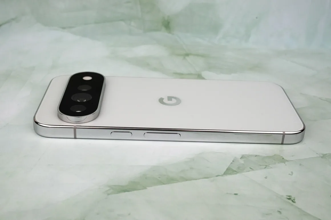 Google Pixel 11 Pro XL İncelemesi: Küçük Ama Anlamlı Bir Adım 20 Arka yüzünde belirgin, kapsül biçimli bir kamera modülü bulunan beyaz bir akıllı telefon, açık yeşil renkli mermer desenli bir yüzey üzerinde duruyor.