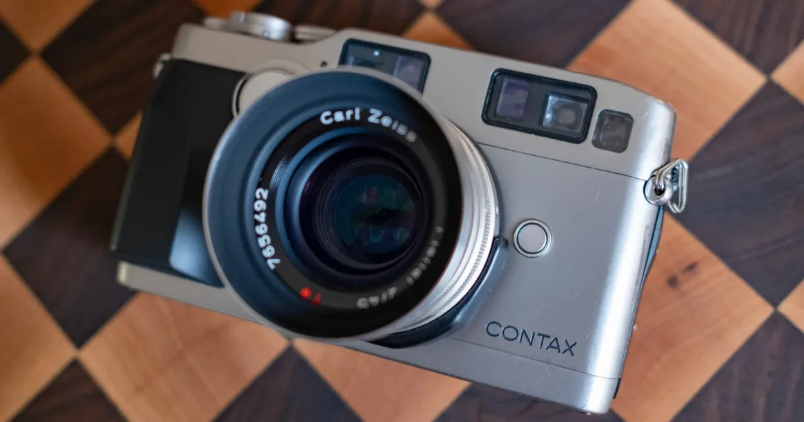 Carl Zeiss objektifli, gümüş renkli bir Contax fotoğraf makinesi ahşap dama desenli bir yüzey üzerinde duruyor.