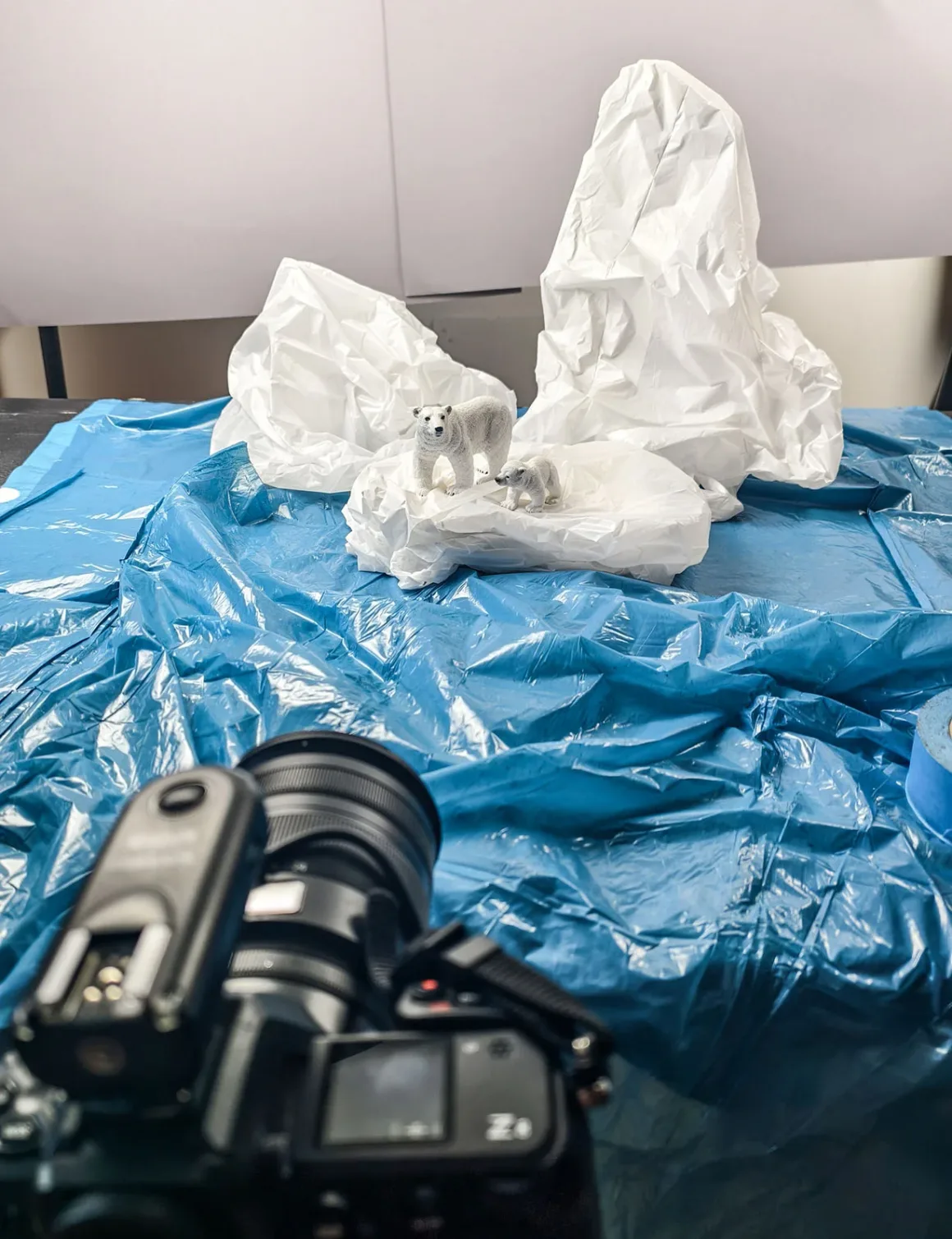 Doğanın Yerini Atıkların Aldığı Bir Dünya: Benedek Lampert'in Yeni Fotoğraf Serisi 9 A camera in the foreground is pointed at a diorama featuring two polar bear figurines on crumpled white paper icebergs set against a blue plastic sheet.