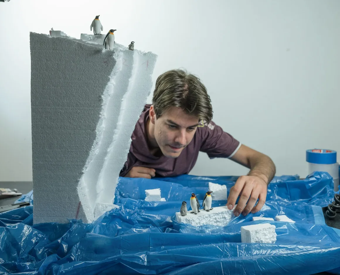 Doğanın Yerini Atıkların Aldığı Bir Dünya: Benedek Lampert'in Yeni Fotoğraf Serisi 13 A man leans over a table covered in blue plastic, arranging small penguin figurines on pieces of white foam that represent icebergs.