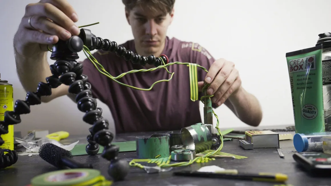 Doğanın Yerini Atıkların Aldığı Bir Dünya: Benedek Lampert'in Yeni Fotoğraf Serisi 14 A person sits at a table assembling a project with green and yellow wires, a flexible tripod, and various metal components.