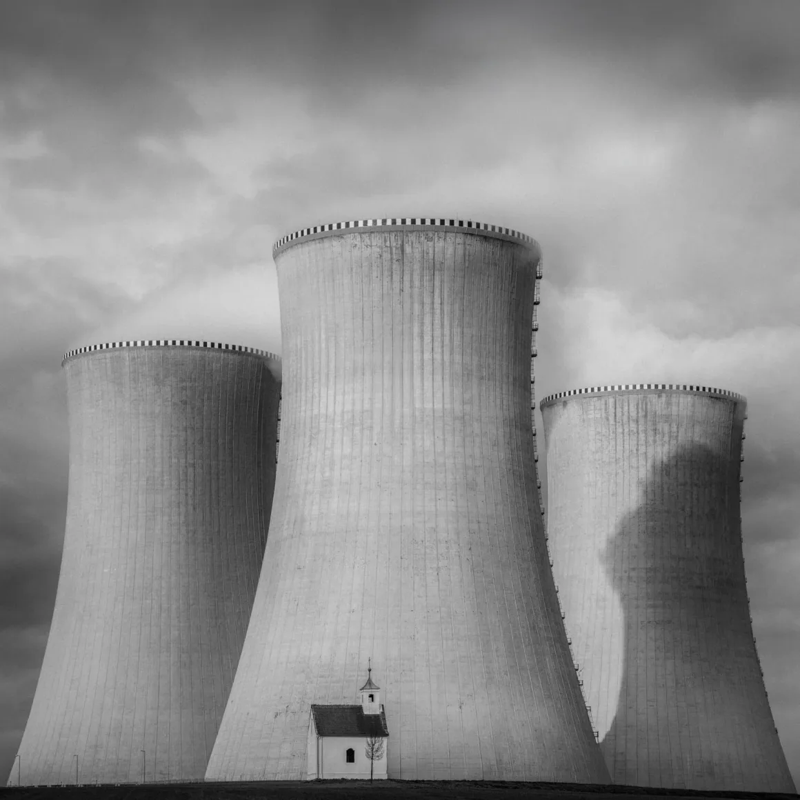 Minimalist Fotoğraf Ödülleri 2026: Kazananlar Sadeliğin Gücünü Gösteriyor 34 A small, white chapel stands in front of three massive, towering concrete cooling towers under a cloudy sky.