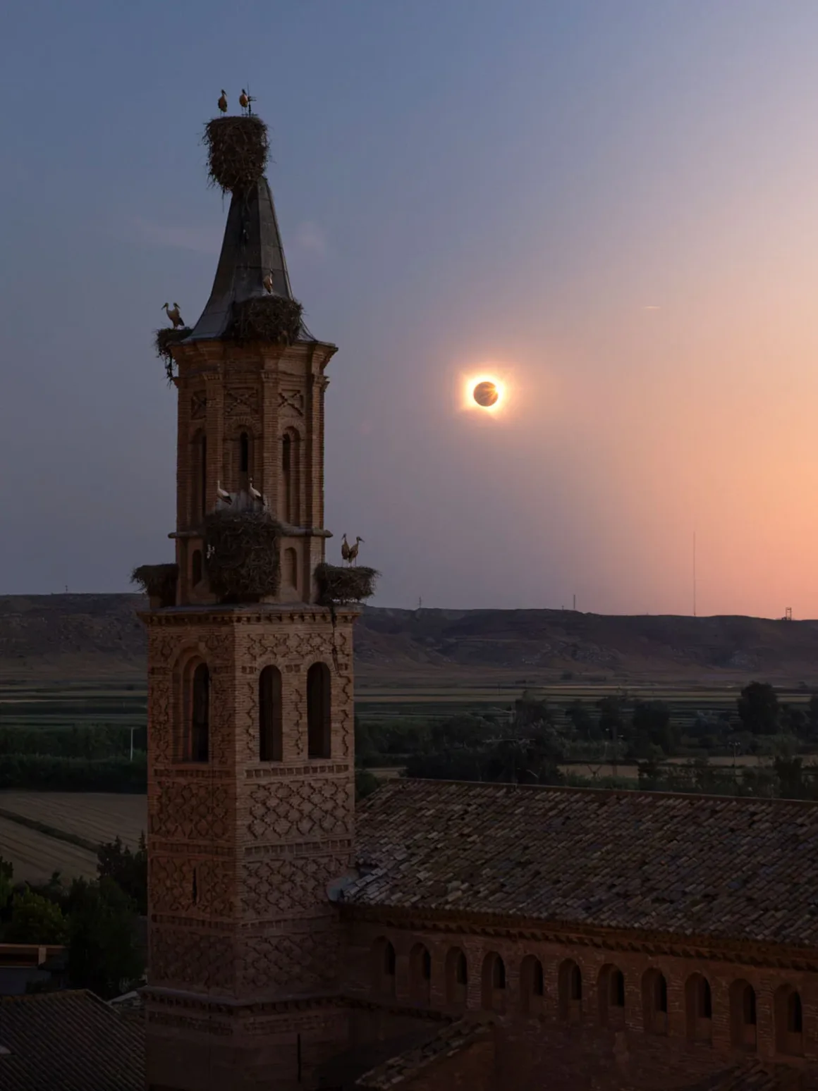 İki Fotoğrafçı Kusursuz Tutulma Karesi İçin Bir Yıl Hazırlandı, Her Şey 30 Saniyeye Kaldı 28 Üzerinde birden fazla leylek yuvası bulunan yüksek ve süslü tuğla kilise kulesi, Güneş tutulmasının görüldüğü gün batımı gökyüzüne karşı yükseliyor.