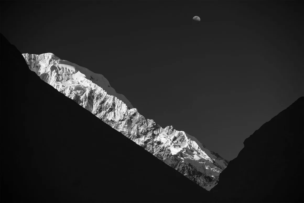 Minimalist Fotoğraf Ödülleri 2026: Kazananlar Sadeliğin Gücünü Gösteriyor 39 A black and white landscape shows a snow-capped mountain peak illuminated against a dark sky with a visible crescent moon.