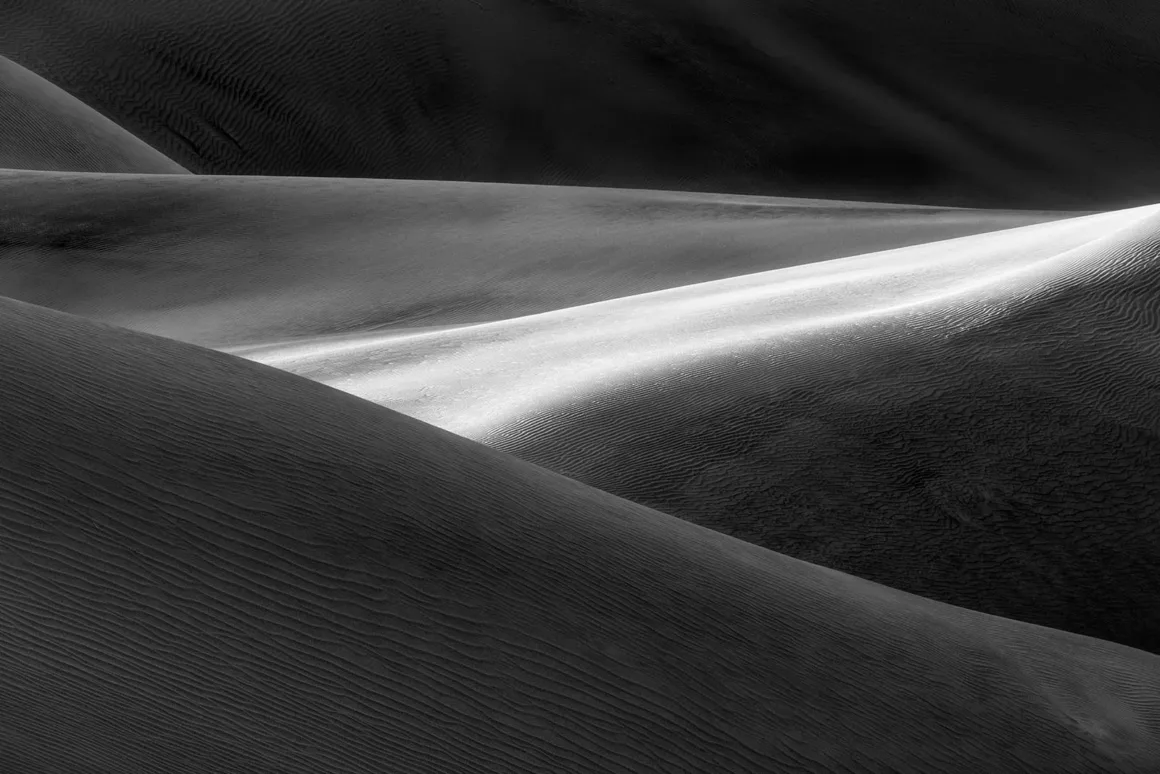 Minimalist Fotoğraf Ödülleri 2026: Kazananlar Sadeliğin Gücünü Gösteriyor 38 A black and white landscape of rolling sand dunes with a bright, sunlit ridge cutting diagonally across the frame.