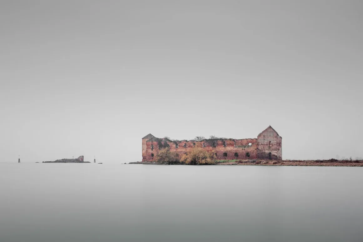 Minimalist Fotoğraf Ödülleri 2026: Kazananlar Sadeliğin Gücünü Gösteriyor 42 A long, ruined brick building sits on a flat, desolate island surrounded by calm, grey water under a hazy, overcast sky.