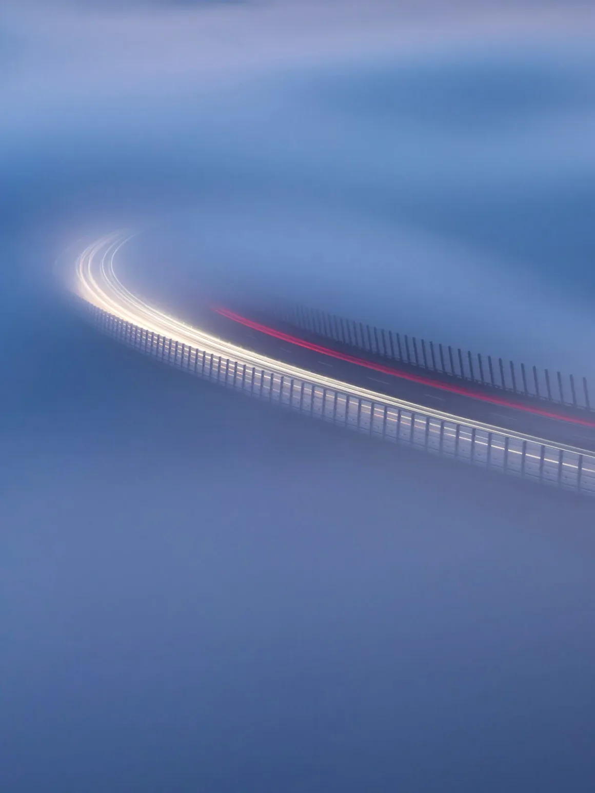 Minimalist Fotoğraf Ödülleri 2026: Kazananlar Sadeliğin Gücünü Gösteriyor 40 A long-exposure shot of a curved bridge at night, with blurred white and red light trails from vehicles moving through thick fog.