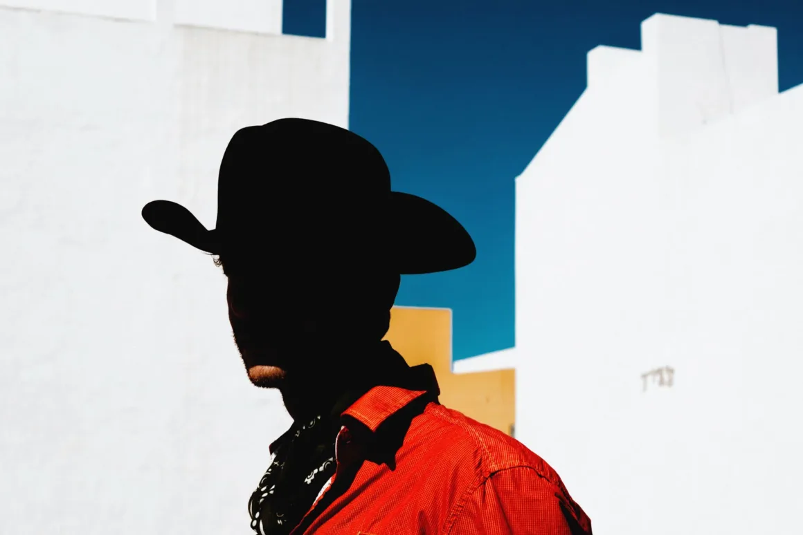 Minimalist Fotoğraf Ödülleri 2026: Kazananlar Sadeliğin Gücünü Gösteriyor 52 A person in a cowboy hat and red shirt stands in silhouette against a bright blue sky and white buildings.