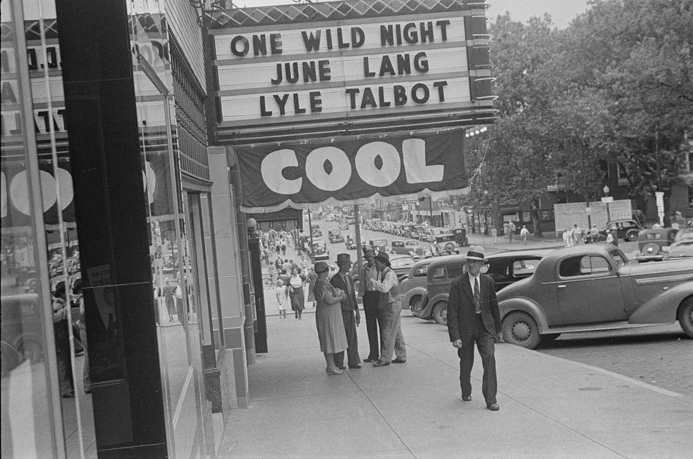 Klimalı Sinemalar Yaz Gişe Filmlerini Nasıl Doğurdu? 20 Bir sinema salonunun önündeki sokak manzarasında, June Lang ve Lyle Talbot’ın başrollerini paylaştığı One Wild Night filminin afişi, altında asılı “SERİN” yazılı pankart ve kaldırımda yürüyen yayalar görülüyor.