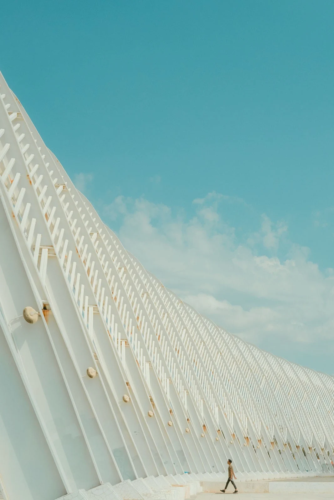 Minimalist Fotoğraf Ödülleri 2026: Kazananlar Sadeliğin Gücünü Gösteriyor 57 A person walks along a paved path beside a large, white, ribbed architectural structure under a clear blue sky.