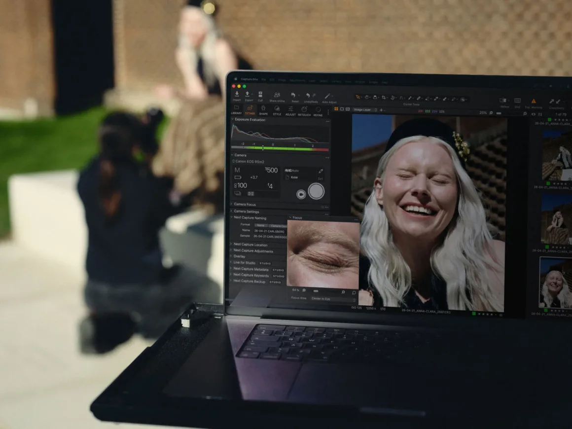 Capture One, İki Canon Kameraya Daha Kablosuz Tethering Getiriyor 17 Capture One açık dizüstü ekranda gülümseyen bir kadının portresi; arka planda fotoğrafçı ve model görülüyor.
