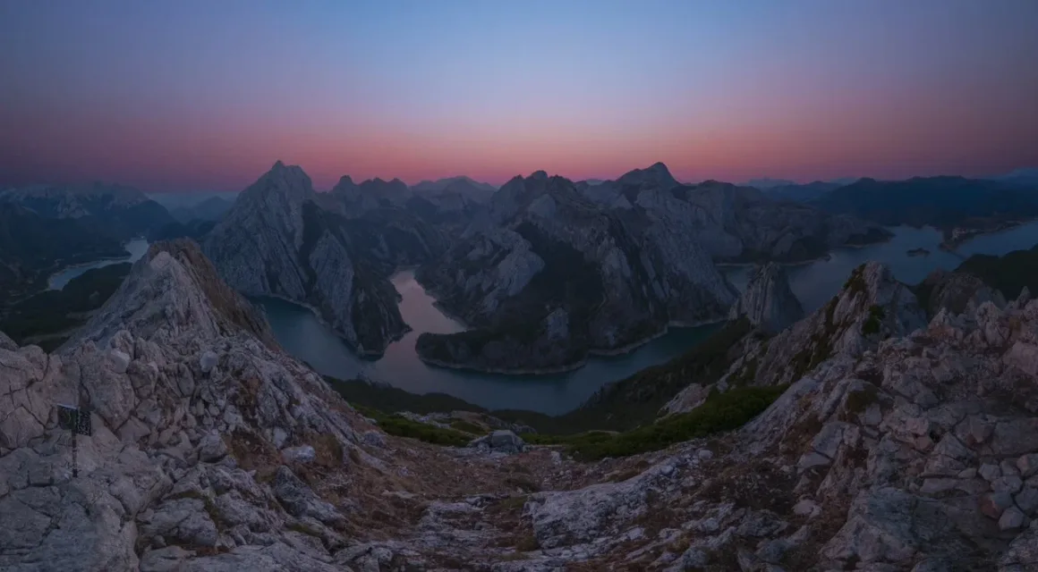 Angel Fux, Tam Güneş Tutulmasını Tek Bir Fotoğrafta Zamana Dönüştürdü 21 A high-angle view of a winding river flowing through a deep valley surrounded by jagged, rocky mountain peaks at twilight.