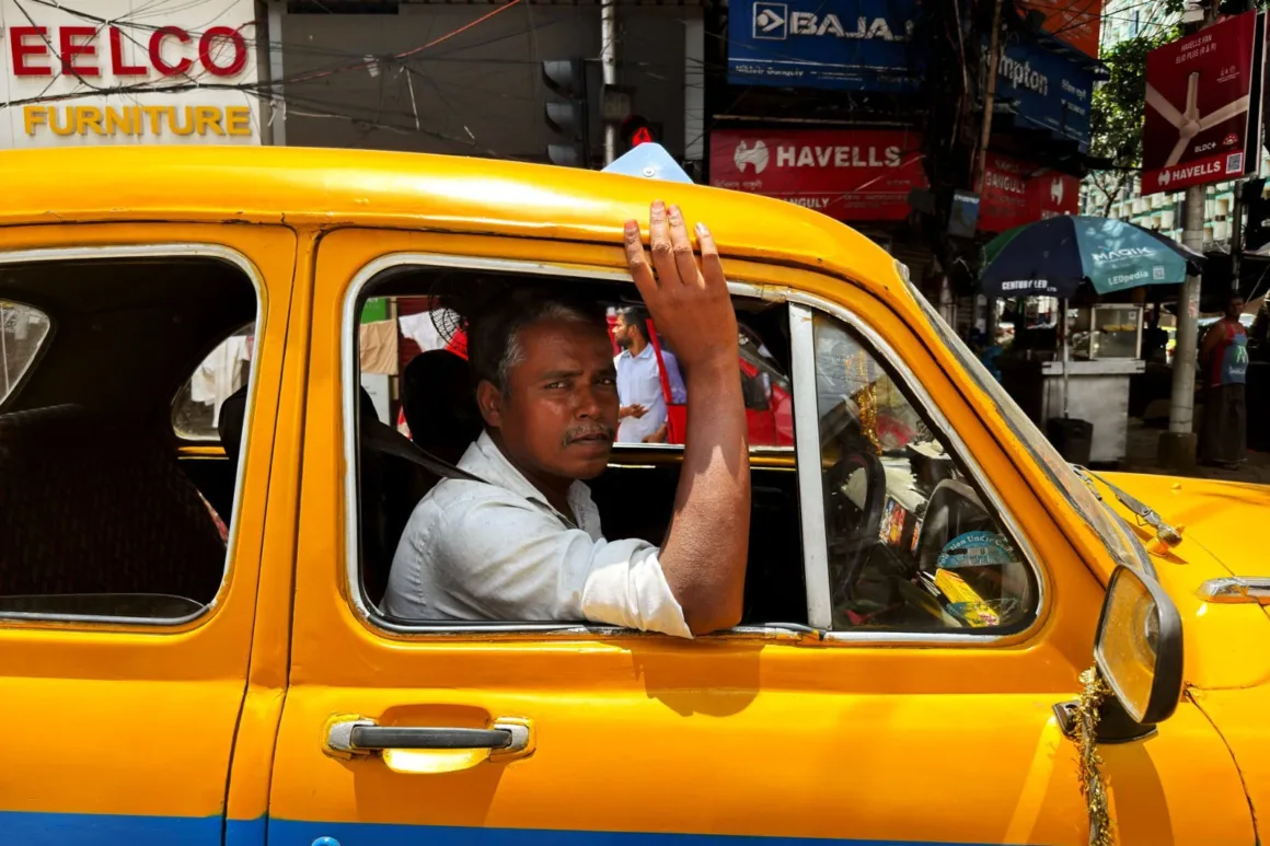 Leica Lux 2.0’a Steve McCurry İmzalı Yeni Görünüm Geldi 22 A man with a mustache sits in the driver's seat of a bright yellow taxi, resting his hand on the roof of the car.