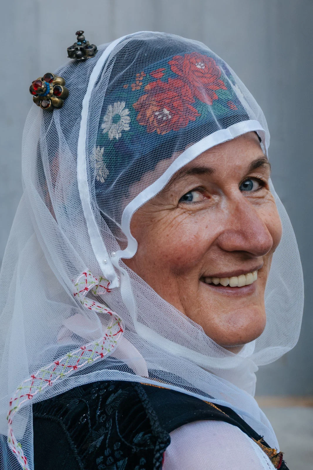 Sony World Photography Awards 2027’ye Katılmanız İçin 15 İlham Verici Fotoğraf 24 A smiling woman with blue eyes wears a traditional headpiece featuring a floral-patterned cap covered by a sheer white veil.