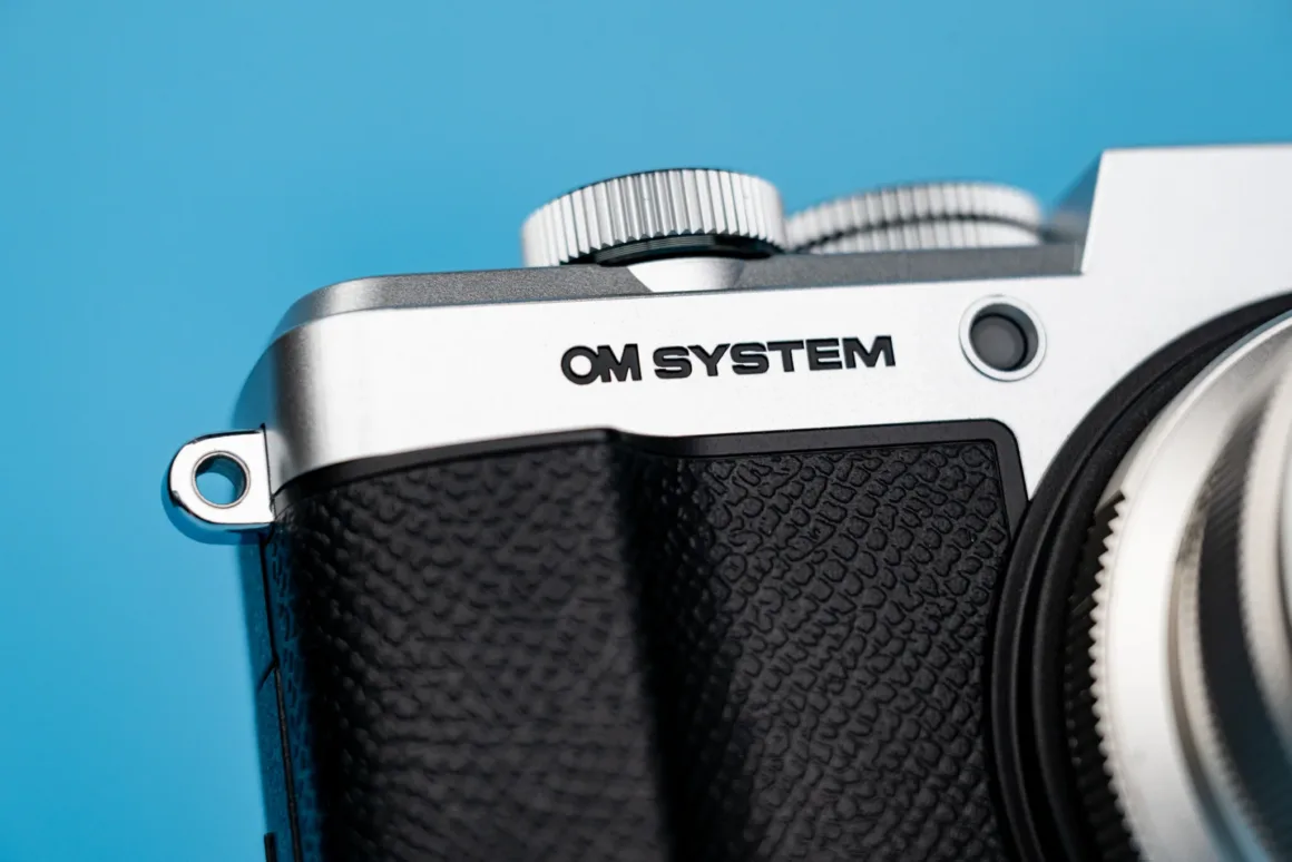 OM System PEN İncelemesi: Tanıdık Ama Son Derece Şık 21 A close-up view of the top corner of a silver and black camera body with the text "OM SYSTEM" printed on the front.