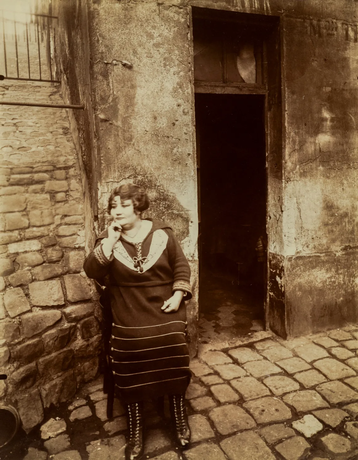Vicente Wolf’un Nadir Fotoğraf Koleksiyonu Açık Artırmaya Çıkıyor 18 Kısa koyu saçlı bir kadın, taş döşeli dar bir sokakta sandalyede oturuyor; çenesini eline dayamış, koyu renk elbise ve bağcıklı botlar giyiyor.