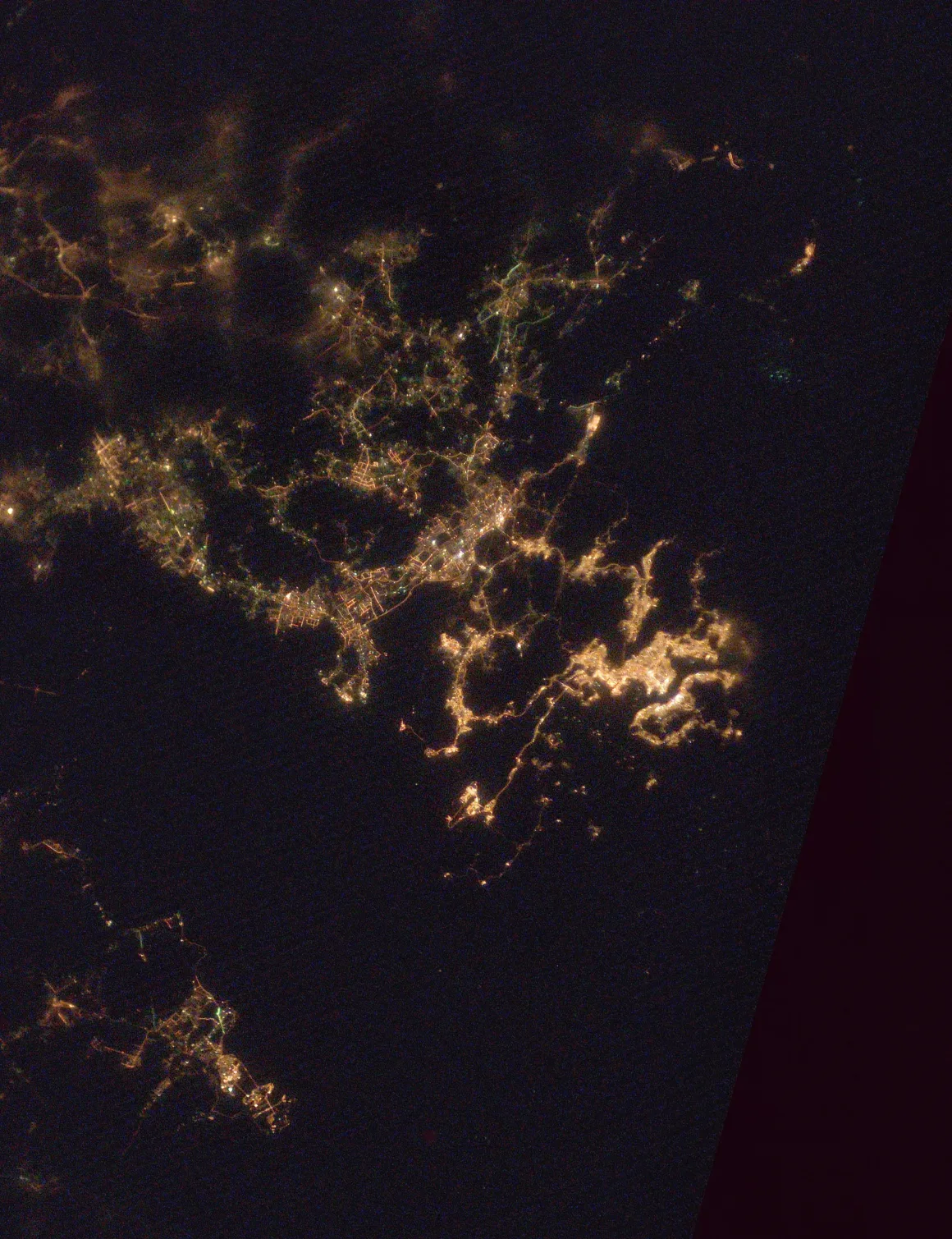 Astronotun Önce-Sonra Fotoğrafları Kentlerin Turuncudan Beyaz Işığa Geçişini Gösteriyor 31 A satellite view of a cluster of city lights at night, showing interconnected urban areas against a dark background.