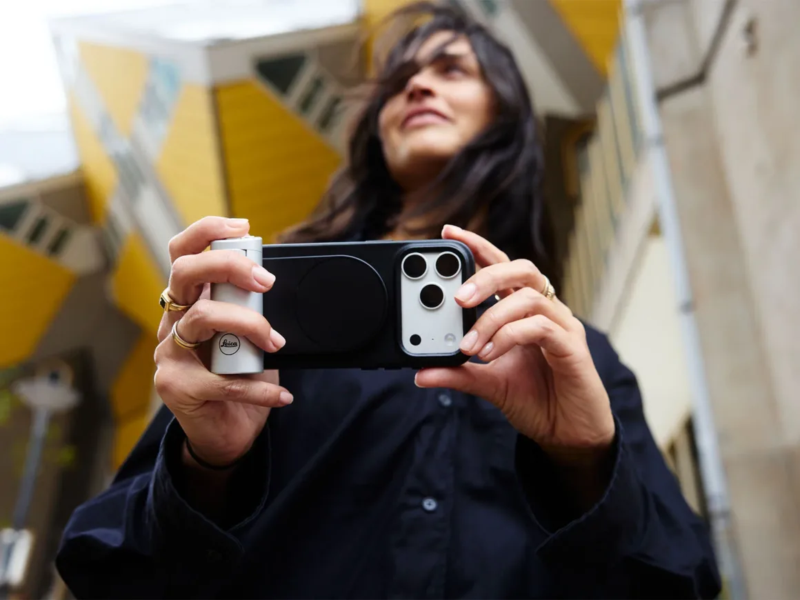 Leica Lux 2.0’a Steve McCurry İmzalı Yeni Görünüm Geldi 28 Bir kişi, görünür Leica logosuna sahip kamera grip’i takılmış bir akıllı telefonu, sarı küp biçimli binaların önünde tutuyor.