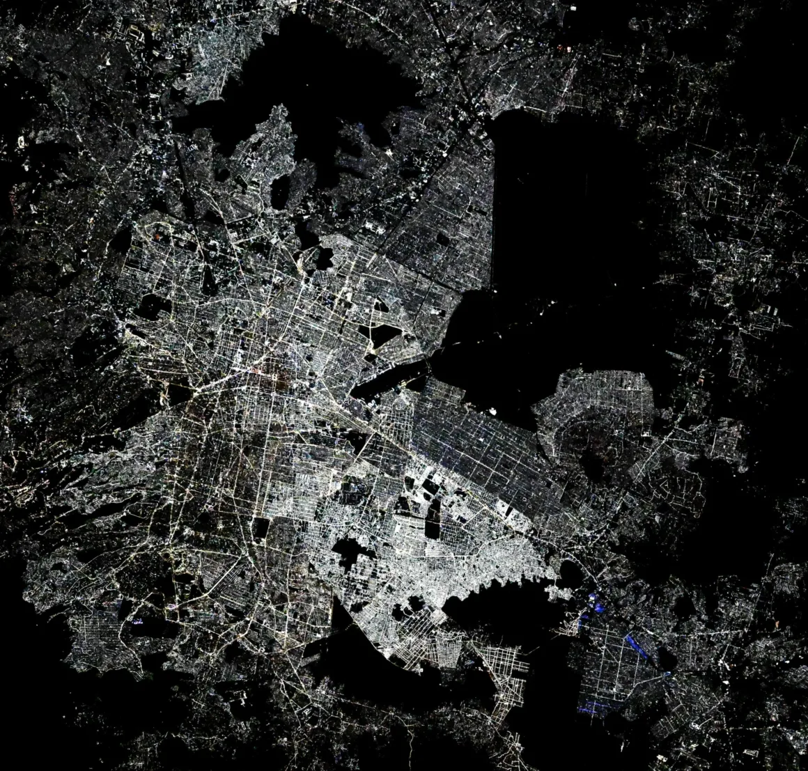 Astronotun Önce-Sonra Fotoğrafları Kentlerin Turuncudan Beyaz Işığa Geçişini Gösteriyor 22 A high-contrast, overhead view of a sprawling city at night, showing a dense grid of illuminated streets and buildings against a dark background.