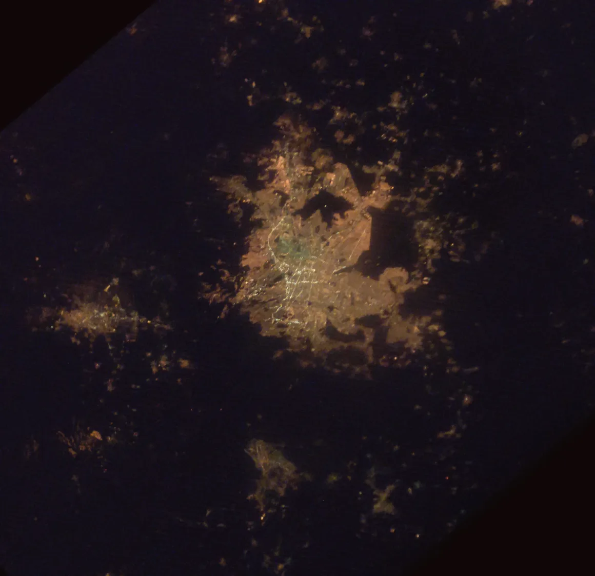 Astronotun Önce-Sonra Fotoğrafları Kentlerin Turuncudan Beyaz Işığa Geçişini Gösteriyor 21 A satellite view of a brightly lit city at night, surrounded by smaller clusters of light against a dark background.