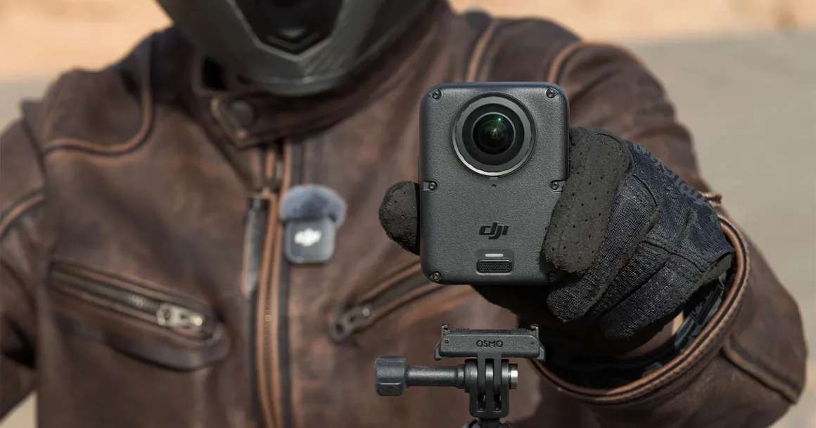 Deri ceket ve motosiklet eldivenleri giyen kişi, üçayağa takılı siyah DJI Osmo aksiyon kamerasını tutuyor.