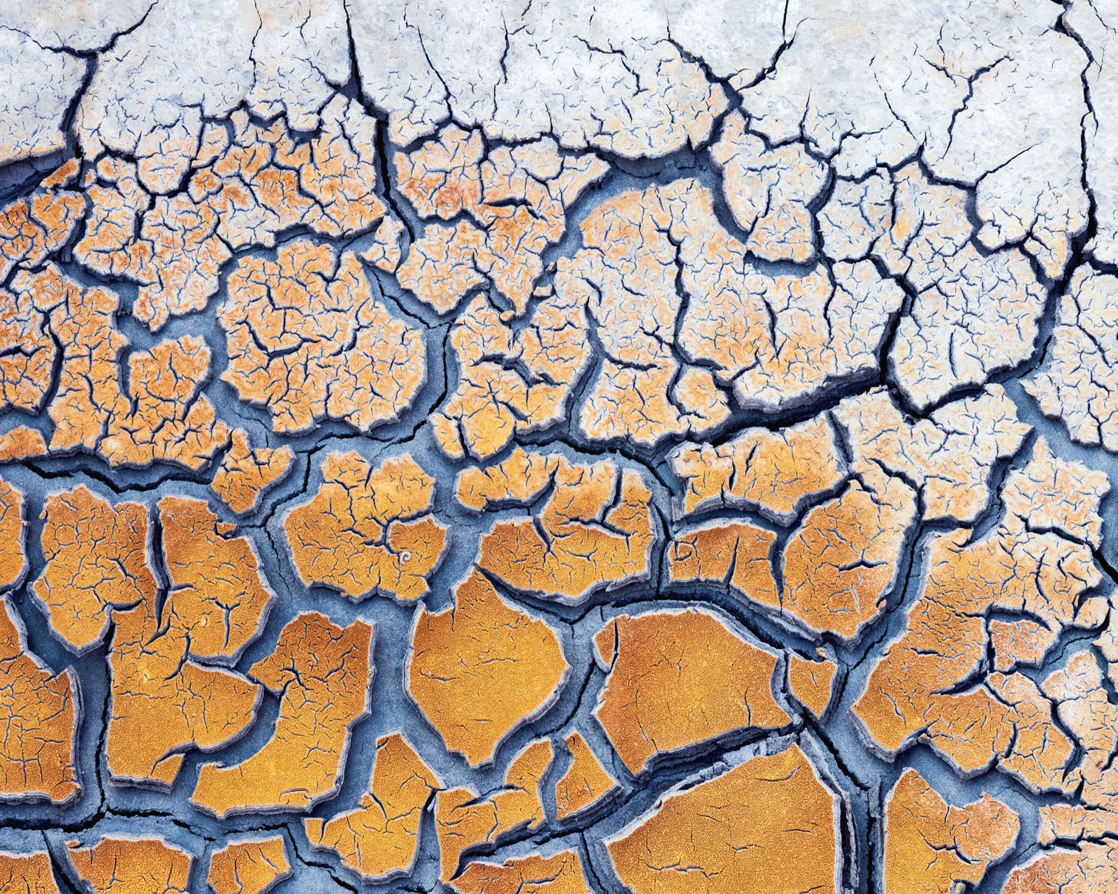 Natural Landscape Photography Awards 2026’nın Kazananları Açıklandı 22 A close-up view of parched, cracked earth with a gradient of orange-brown soil transitioning to light gray at the top.
