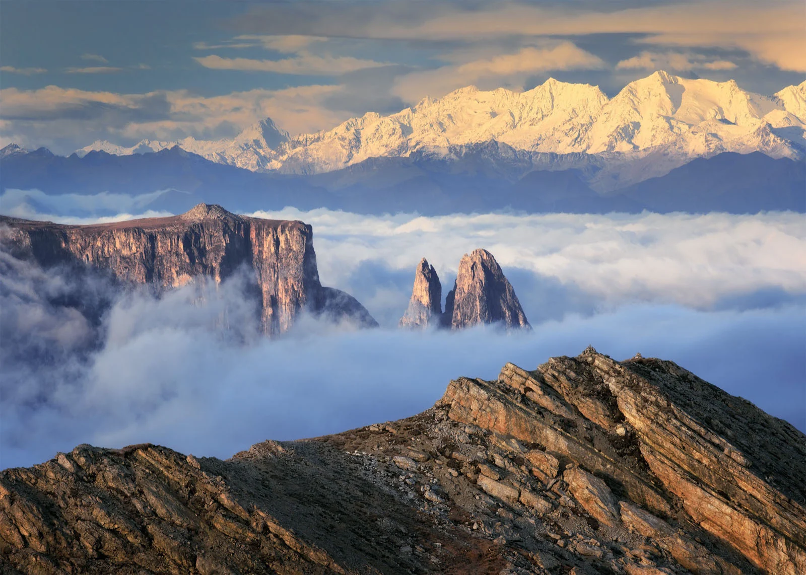 Natural Landscape Photography Awards 2026’nın Kazananları Açıklandı 26 A high-angle view of jagged, rocky mountain peaks rising above a thick layer of clouds, with snow-capped mountains in the distance.
