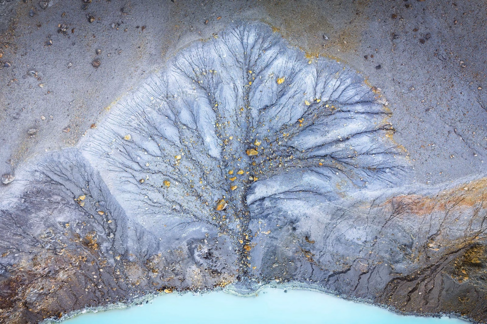 Natural Landscape Photography Awards 2026’nın Kazananları Açıklandı 42 An aerial view shows a dendritic drainage pattern of dark, branching channels carved into grey, rocky terrain leading to a turquoise pool of water.