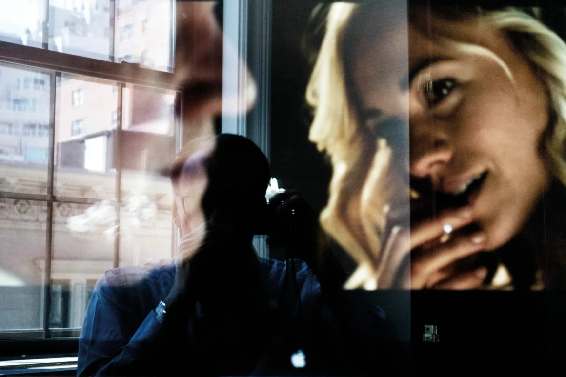 Nicolas Rachline’ın Tekinsiz Fotoğraflarında Modern Yaşamın Yalnızlığı ve Güzelliği 23 Çift pozlamada pencere önünde fotoğraf makinesi tutan kişiyle gülümseyen bir kadının yakın plan portresi üst üste geliyor.