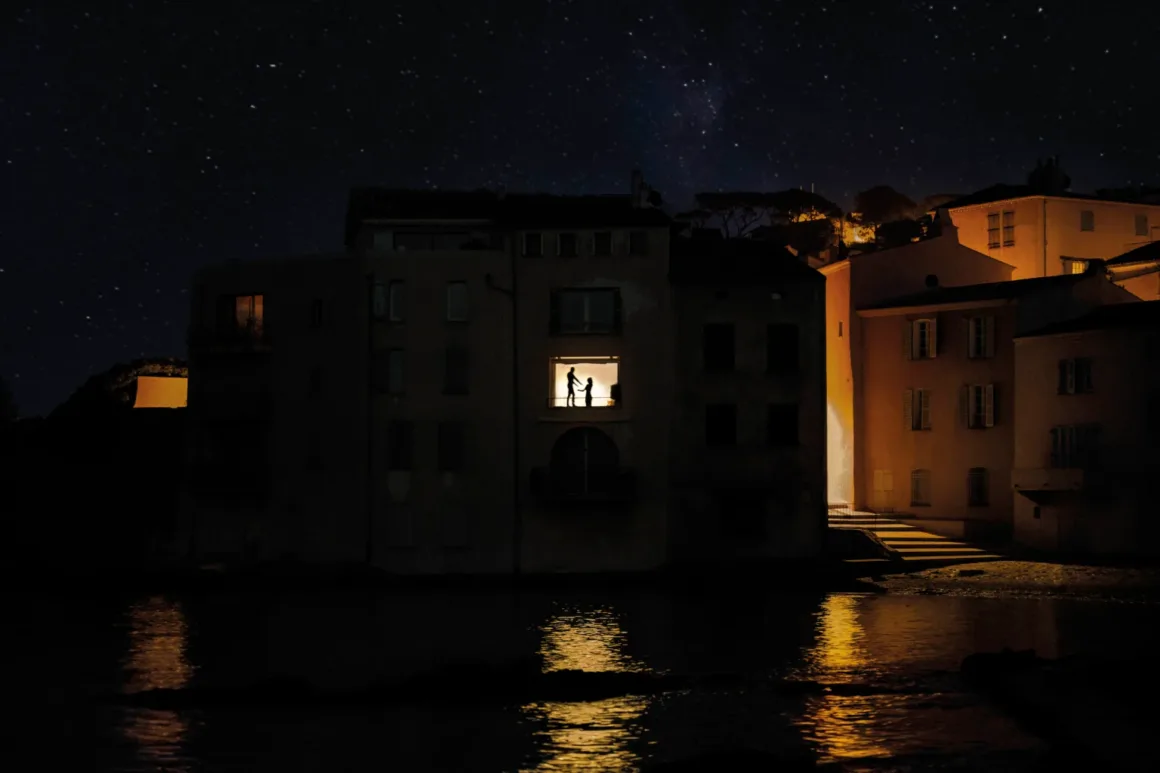Nicolas Rachline’ın Tekinsiz Fotoğraflarında Modern Yaşamın Yalnızlığı ve Güzelliği 18 Yıldızlı bir gecede suya bakan karanlık bir binanın aydınlık penceresinde duran bir çift.