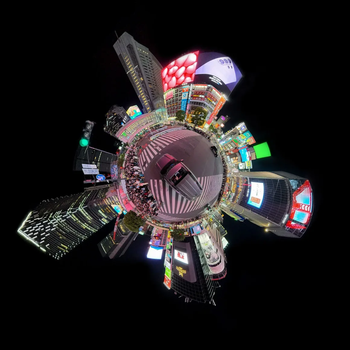 A 360-degree panoramic view of a busy city intersection at night, featuring tall buildings with bright digital billboards surrounding a central crosswalk.