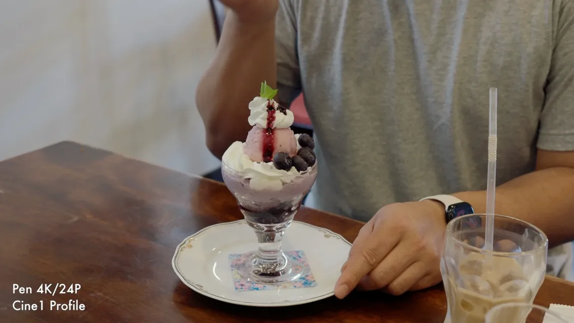 OM System PEN İncelemesi: Tanıdık Ama Son Derece Şık 38 A person sits at a wooden table next to a blueberry parfait in a glass dish and a glass of iced coffee.